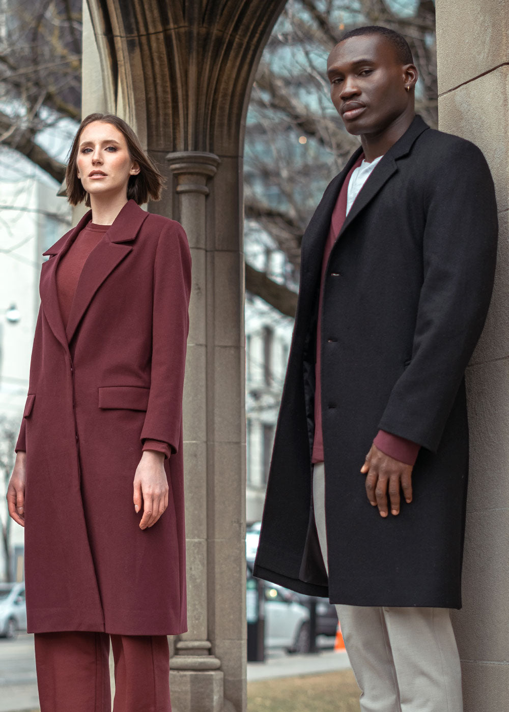 Men and women wearing premium winter outerwear by Zeitgeist, including a structured burgundy wool coat with notch lapels and a classic black tailored overcoat.
